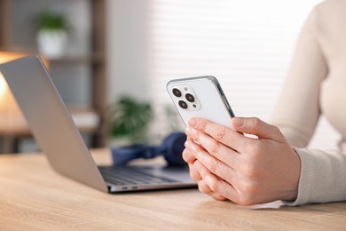 Photo of Woman using modern smartphone at wooden table indoors, closeup
