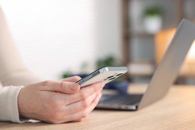 Photo of Woman using modern smartphone at wooden table indoors, closeup