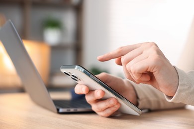 Photo of Woman using modern smartphone at wooden table indoors, closeup