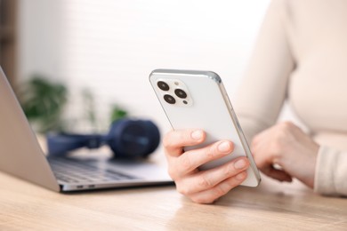 Photo of Woman using modern smartphone at wooden table indoors, closeup