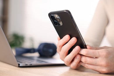 Photo of Woman using modern smartphone at wooden table indoors, closeup