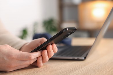 Photo of Woman using modern smartphone at wooden table indoors, closeup