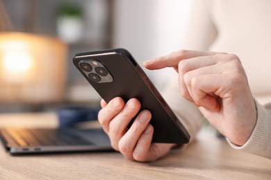 Photo of Woman using modern smartphone at wooden table indoors, closeup