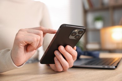 Photo of Woman using modern smartphone at wooden table indoors, closeup