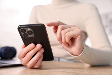 Photo of Woman using modern smartphone at wooden table indoors, closeup