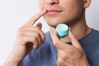 Photo of Young man applying lip balm onto his lips on light grey background, closeup