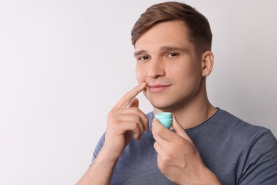 Photo of Young man applying lip balm onto his lips on light grey background, space for text