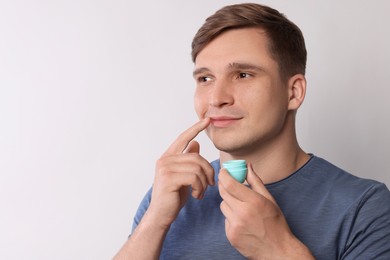 Photo of Young man applying lip balm onto his lips on light grey background, space for text