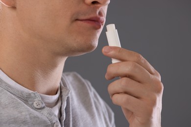 Photo of Young man applying lip balm onto his lips on grey background, closeup