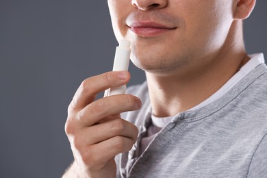 Photo of Young man applying lip balm onto his lips on grey background, closeup