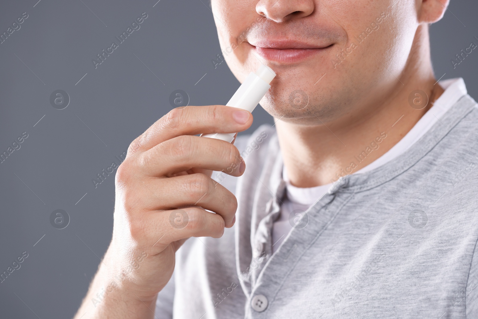 Young man applying lip balm onto his lips on grey background, closeup Photo of Young man applying lip balm onto his lips on grey background, closeup