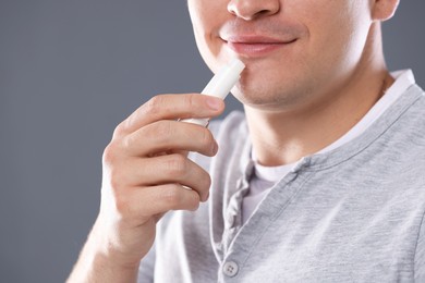 Photo of Young man applying lip balm onto his lips on grey background, closeup