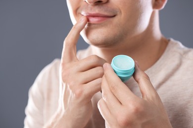 Photo of Young man applying lip balm onto his lips on grey background, closeup