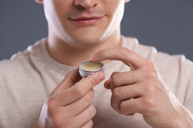 Photo of Young man applying lip balm onto his lips on grey background, closeup