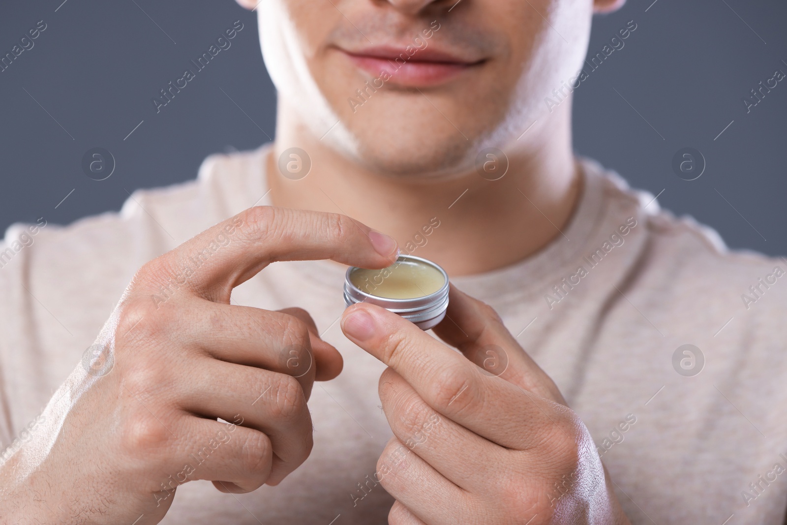Young man applying lip balm onto his lips on grey background, closeup Photo of Young man applying lip balm onto his lips on grey background, closeup