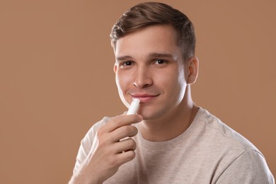Photo of Young man applying lip balm onto his lips on light brown background