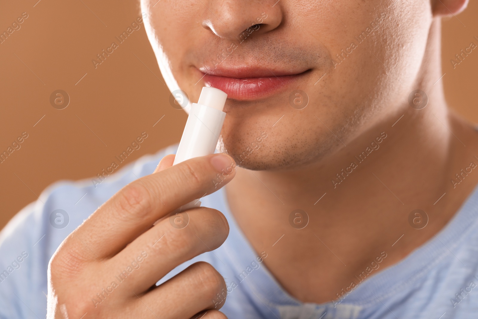 Young man applying lip balm onto his lips on light brown background, closeup Photo of Young man applying lip balm onto his lips on light brown background, closeup