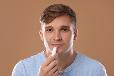 Photo of Young man applying lip balm onto his lips on light brown background