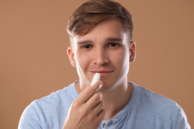 Photo of Young man applying lip balm onto his lips on light brown background