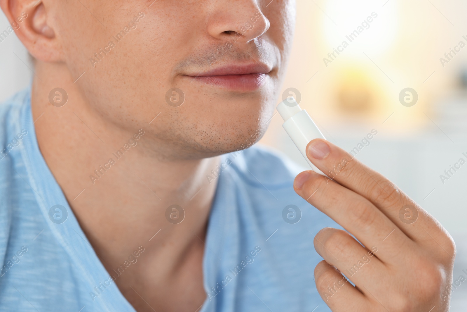 Young man applying lip balm onto his lips at home, closeup Photo of Young man applying lip balm onto his lips at home, closeup