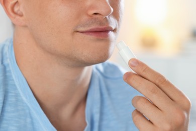 Photo of Young man applying lip balm onto his lips at home, closeup