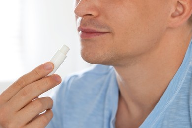 Photo of Young man applying lip balm onto his lips at home, closeup