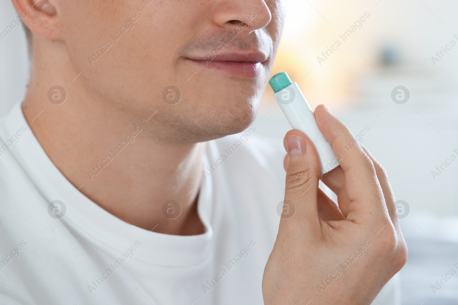 Young man applying lip balm onto his lips at home, closeup Photo of Young man applying lip balm onto his lips at home, closeup