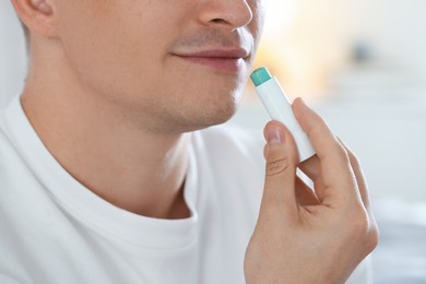 Photo of Young man applying lip balm onto his lips at home, closeup