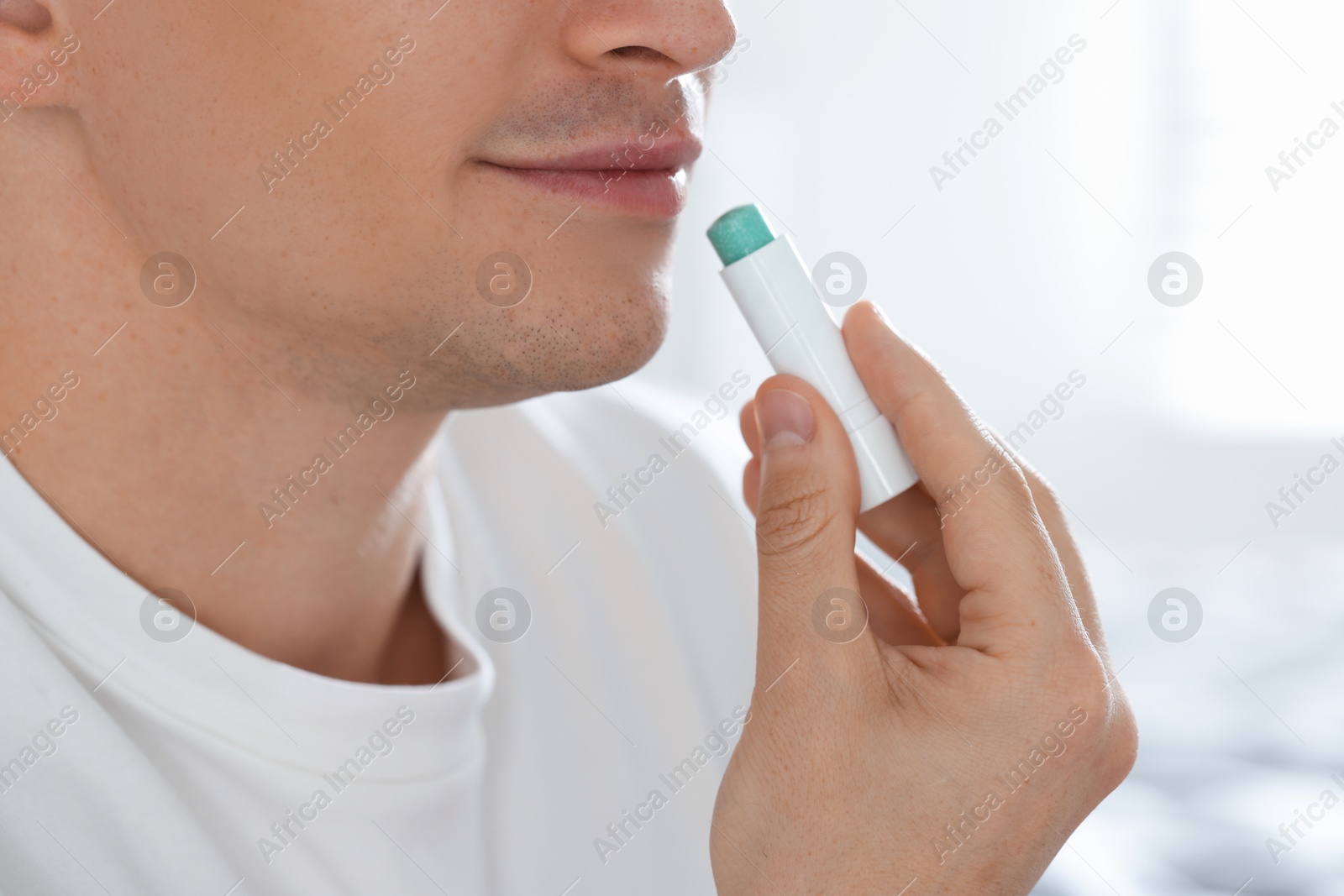 Young man applying lip balm onto his lips at home, closeup Photo of Young man applying lip balm onto his lips at home, closeup