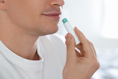 Photo of Young man applying lip balm onto his lips at home, closeup