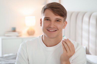 Photo of Young man with cosmetic lip balm at home