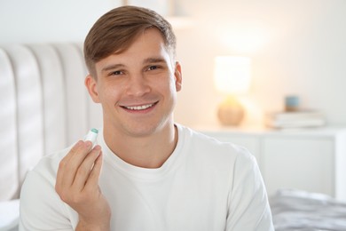 Photo of Young man with cosmetic lip balm at home