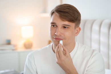 Photo of Young man applying lip balm onto his lips at home