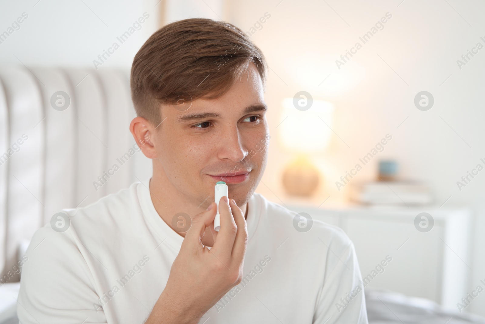 Young man applying lip balm onto his lips at home Photo of Young man applying lip balm onto his lips at home