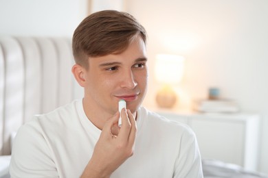 Photo of Young man applying lip balm onto his lips at home