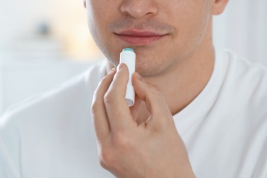 Photo of Young man applying lip balm onto his lips at home, closeup