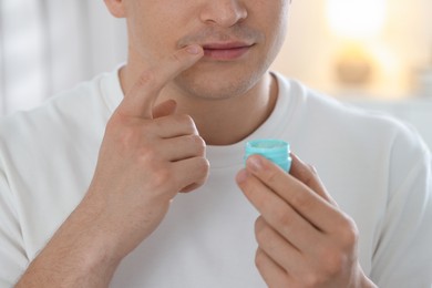 Photo of Young man applying lip balm onto his lips at home, closeup