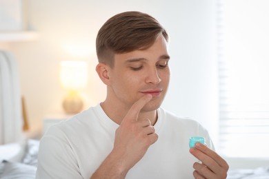 Photo of Young man applying lip balm onto his lips at home
