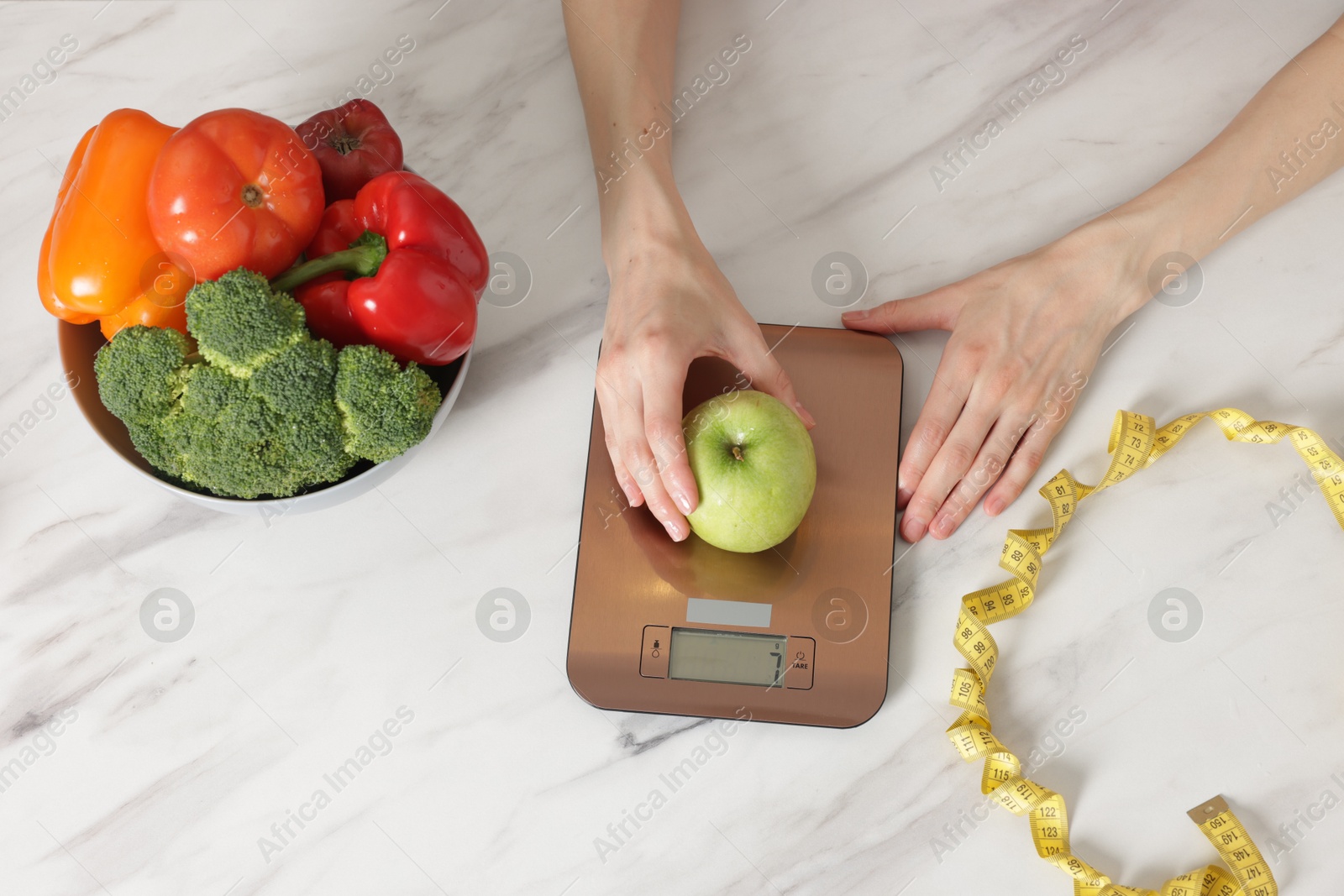 Woman weighting apple on kitchen scale at white marble table, top view Photo of Woman weighting apple on kitchen scale at white marble table, top view