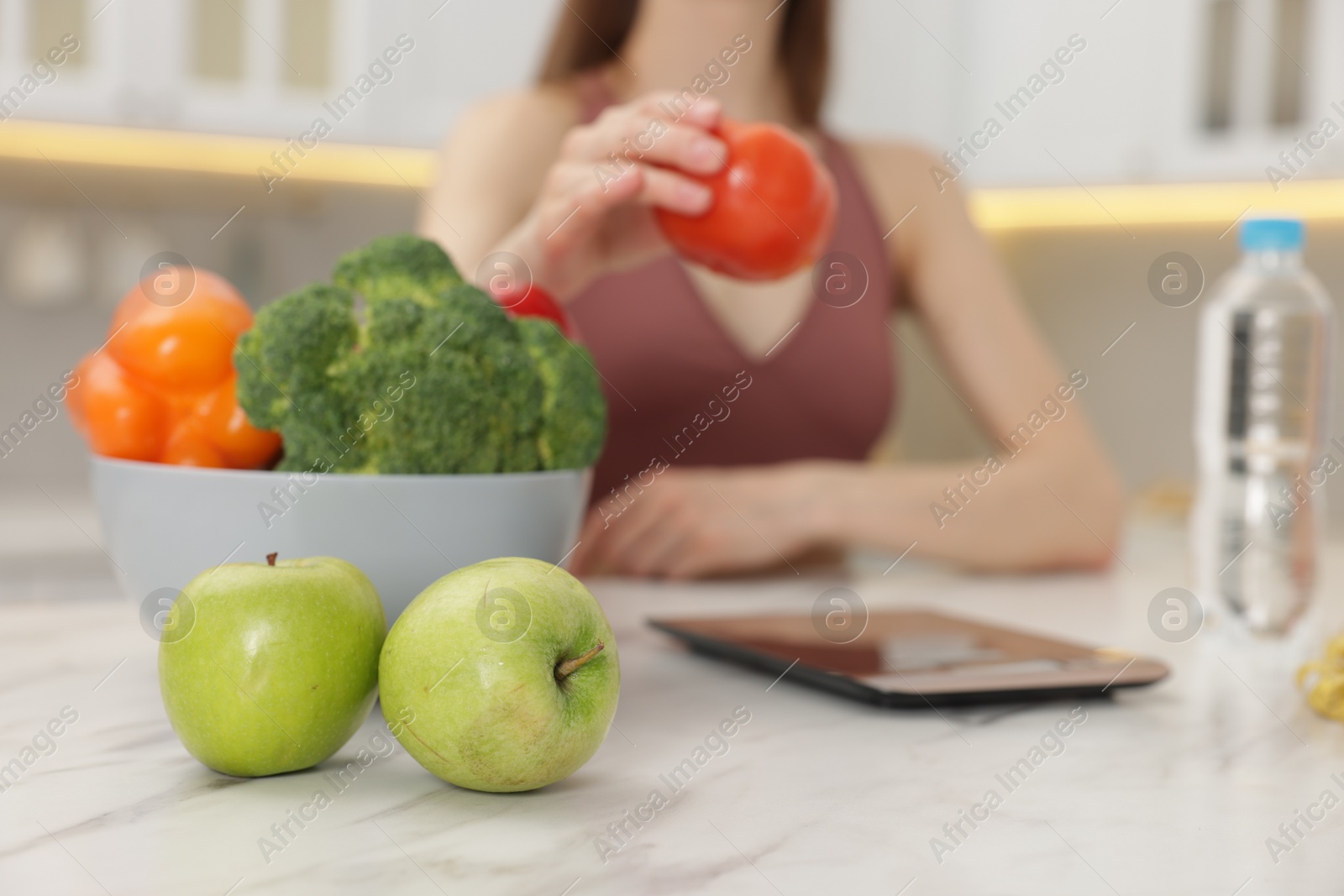 Woman weighting tomato on kitchen scale at white marble table indoors, selective focus Photo of Woman weighting tomato on kitchen scale at white marble table indoors, selective focus
