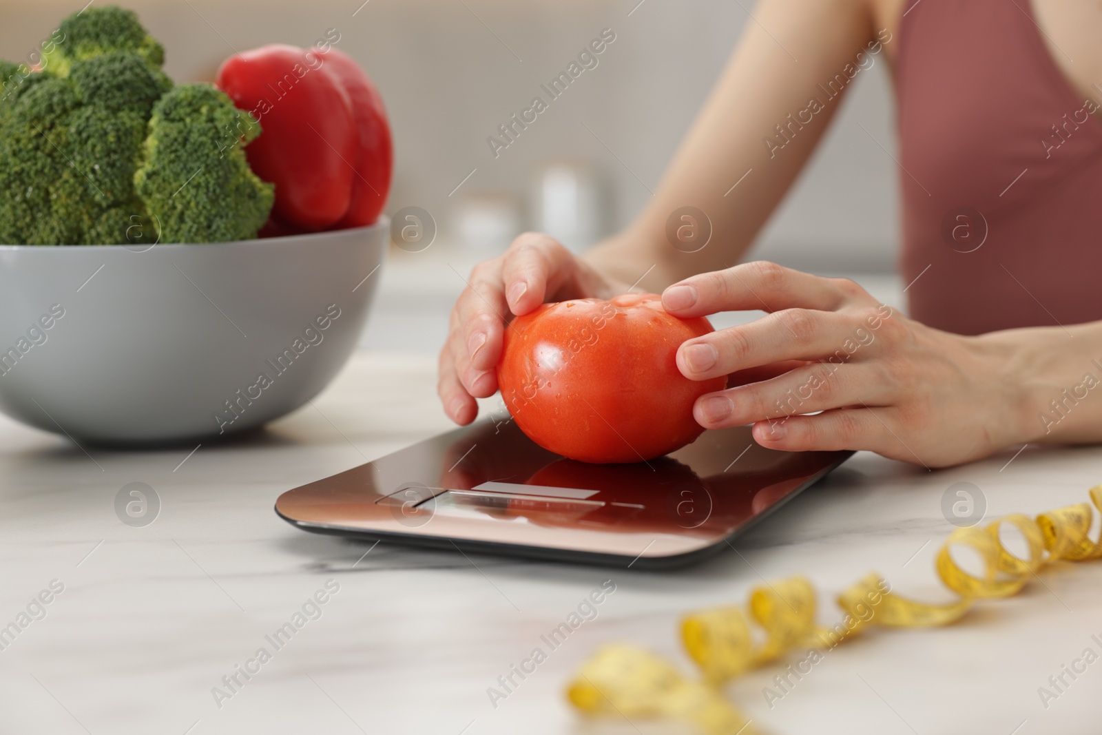 Woman weighting tomato on kitchen scale at white marble table indoors, closeup Photo of Woman weighting tomato on kitchen scale at white marble table indoors, closeup