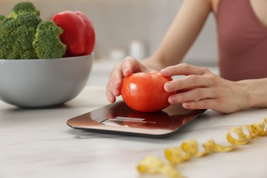 Photo of Woman weighting tomato on kitchen scale at white marble table indoors, closeup