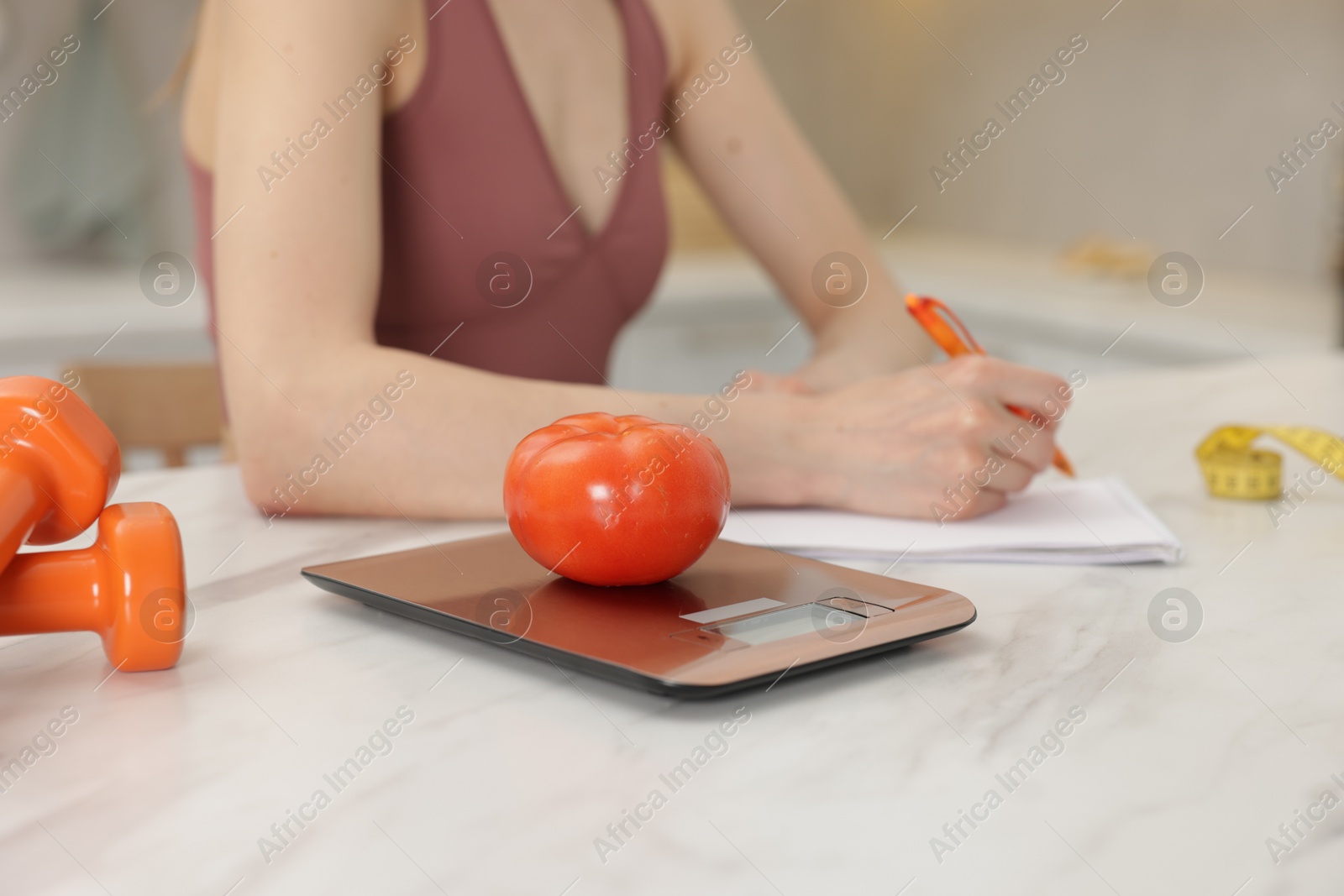 Woman developing diet plan at white marble table indoors, focus on kitchen scale and tomato Photo of Woman developing diet plan at white marble table indoors, focus on kitchen scale and tomato