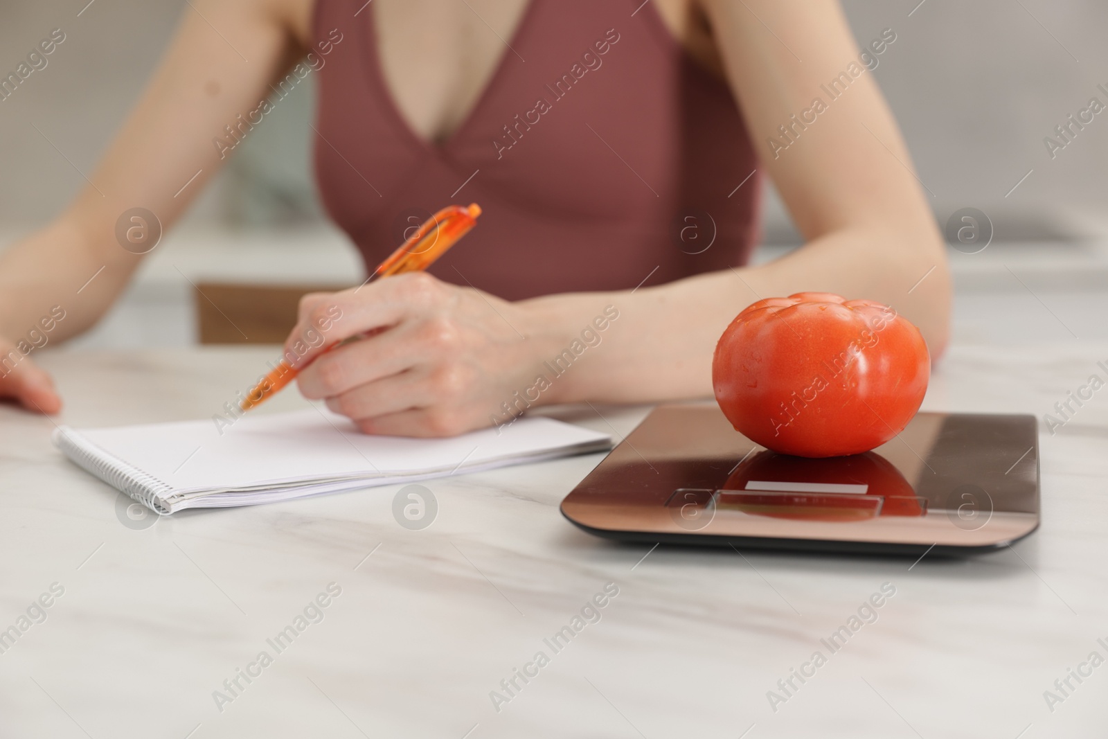 Woman developing diet plan at white marble table indoors, focus on kitchen scale and tomato Photo of Woman developing diet plan at white marble table indoors, focus on kitchen scale and tomato