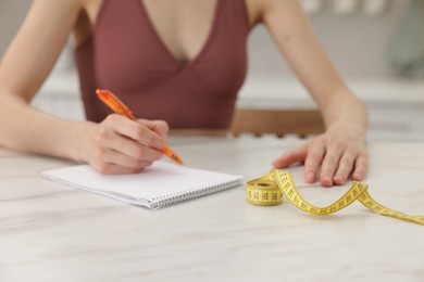 Photo of Woman developing diet plan at white marble table indoors, closeup