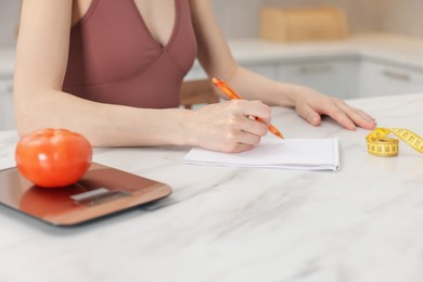 Photo of Woman developing diet plan at white marble table indoors, closeup
