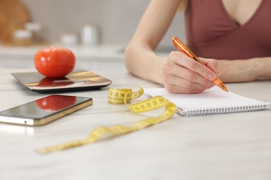 Photo of Woman developing diet plan at white marble table indoors, closeup