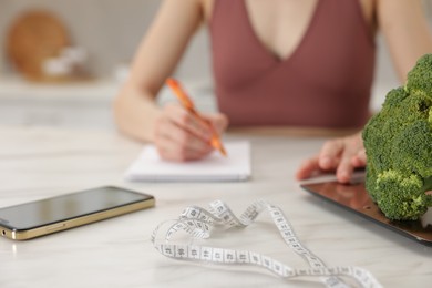 Photo of Woman developing diet plan at white marble table indoors, selective focus