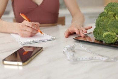 Photo of Woman developing diet plan at white marble table indoors, closeup