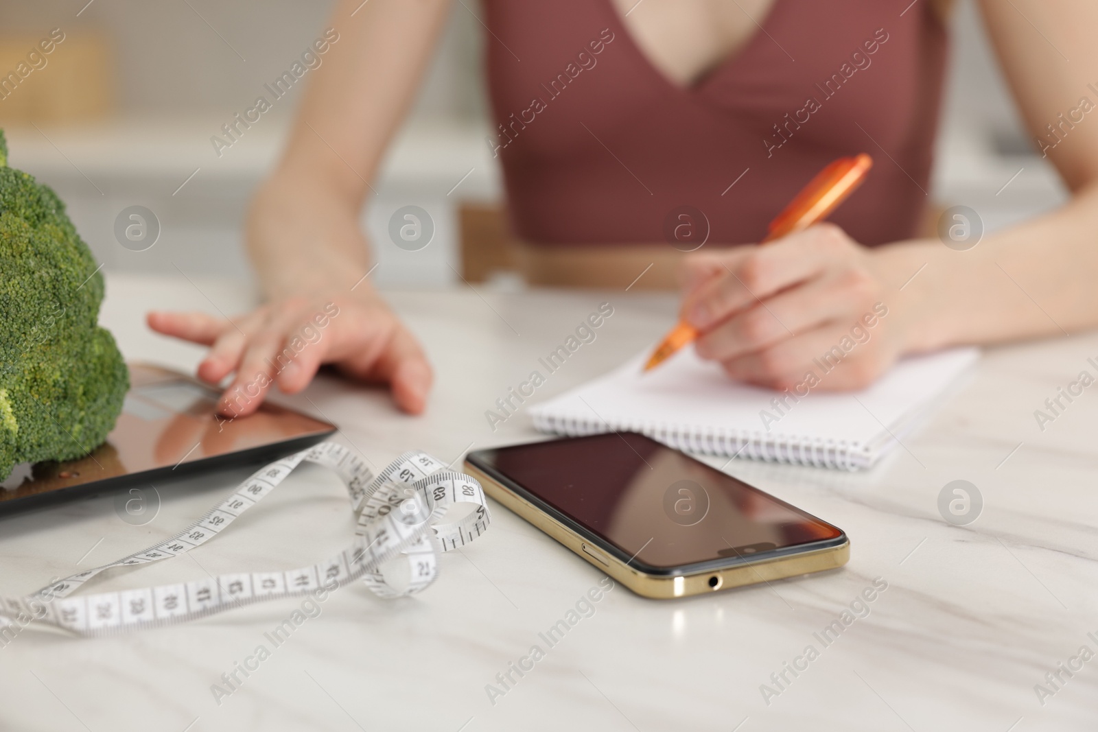 Woman developing diet plan while weighting broccoli on kitchen scale at white marble table indoors, closeup Photo of Woman developing diet plan while weighting broccoli on kitchen scale at white marble table indoors, closeup